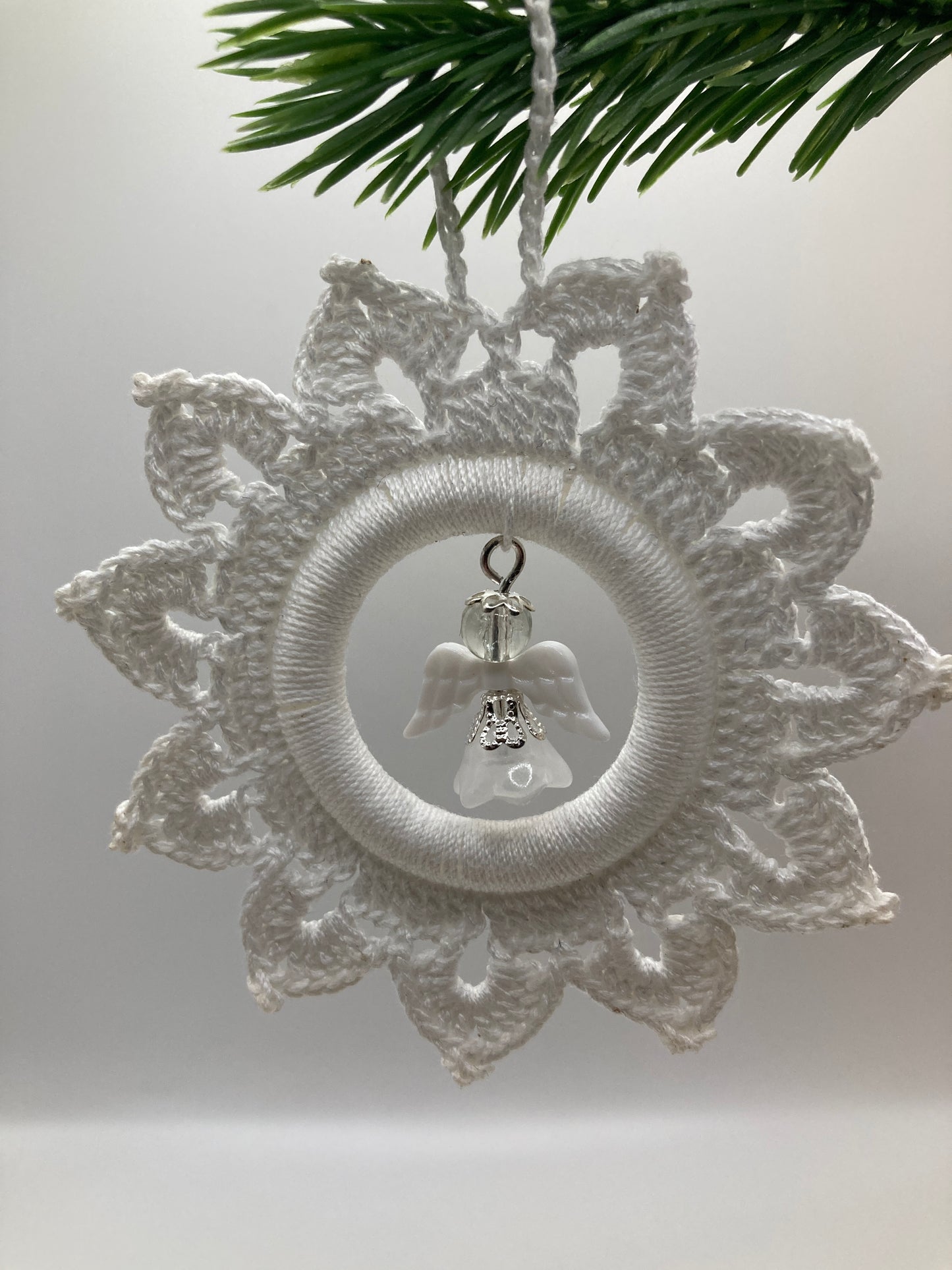 Weißer Häkelstern mit Engel hängt an grünem Tannenzweig