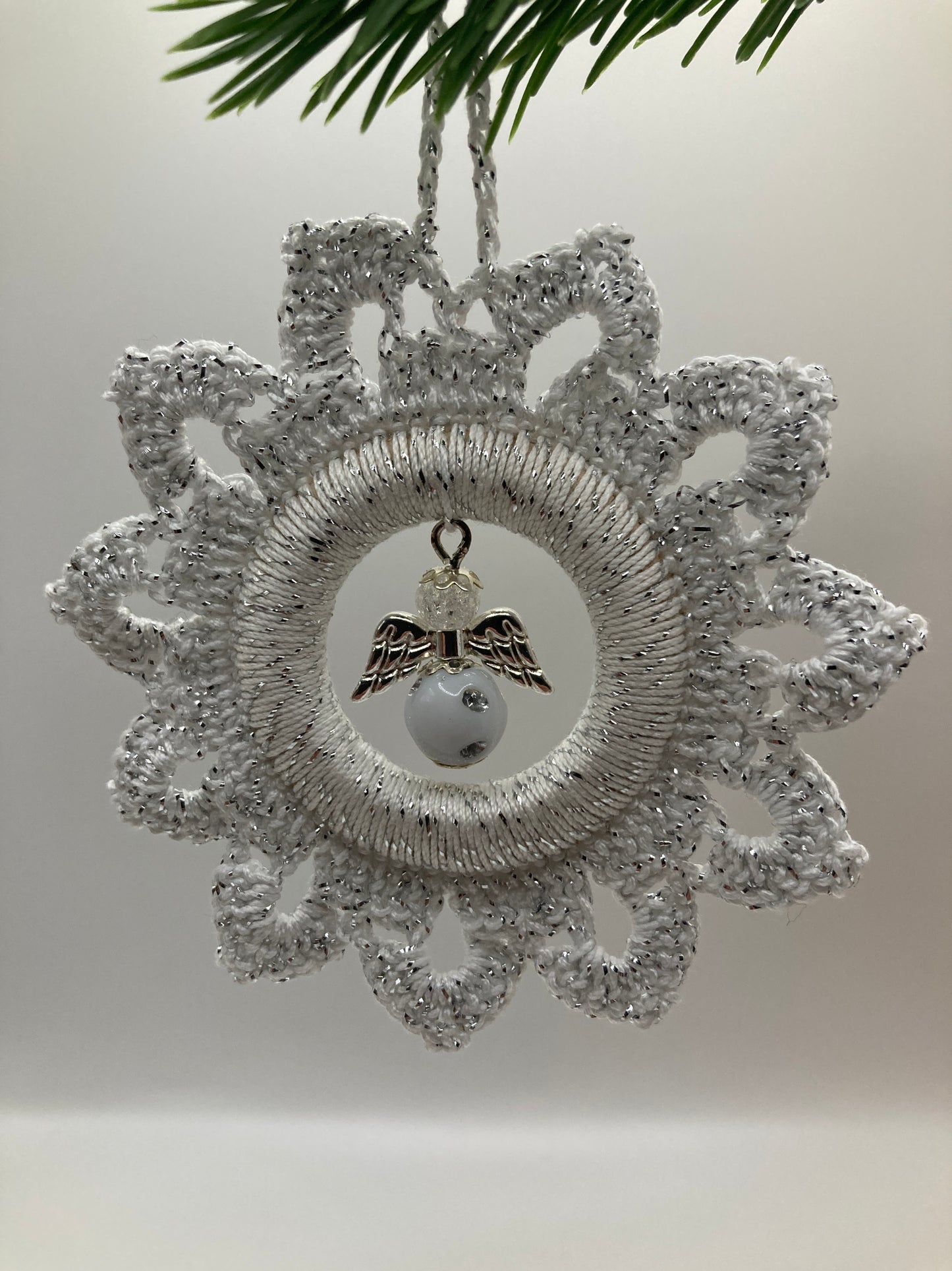 Weißer Häkelstern mit Engel hängt an grünem Tannenzweig