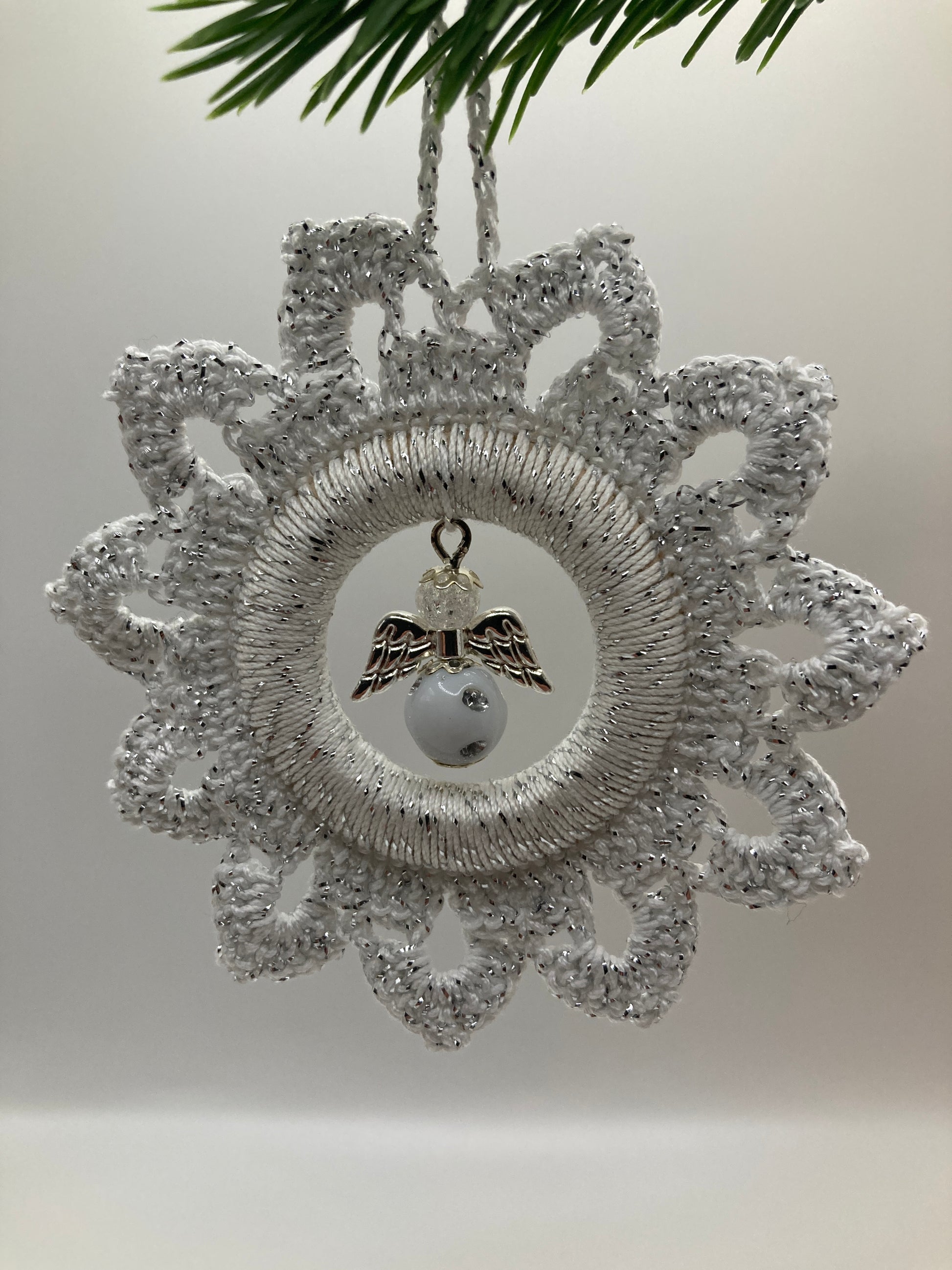 Weißer Häkelstern mit Engel hängt an grünem Tannenzweig