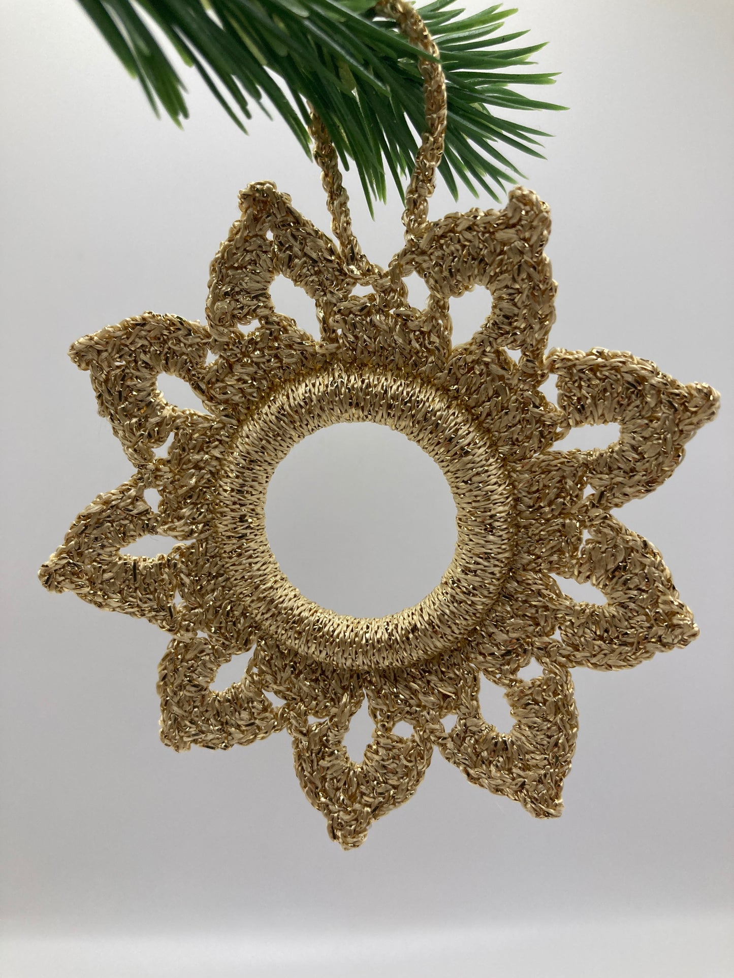 Goldener Häkelstern hängt an grünem Tannenzweig